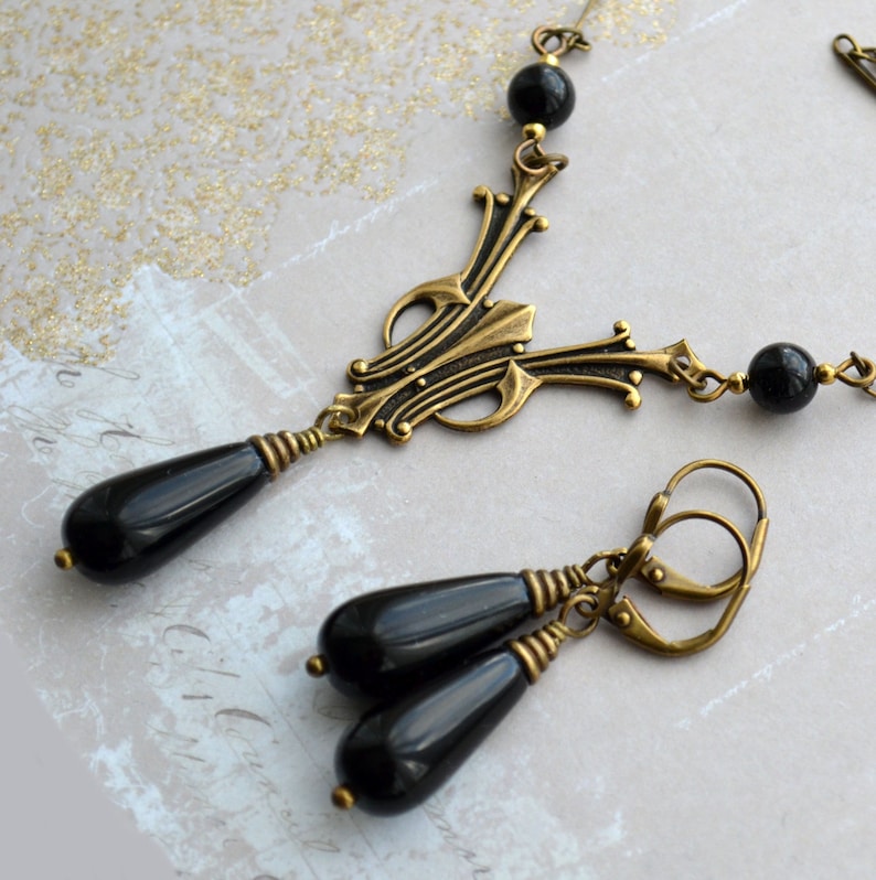 May include: A black and gold necklace and earrings set with a decorative pendant and teardrop-shaped black onyx beads.