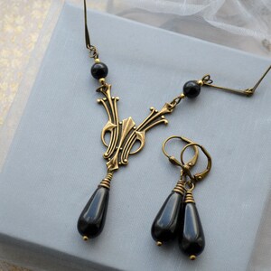 May include: A black onyx necklace and earrings set with a gold-toned pendant featuring an intricate design. The pendant is shaped like a teardrop and hangs from a chain with black onyx beads.