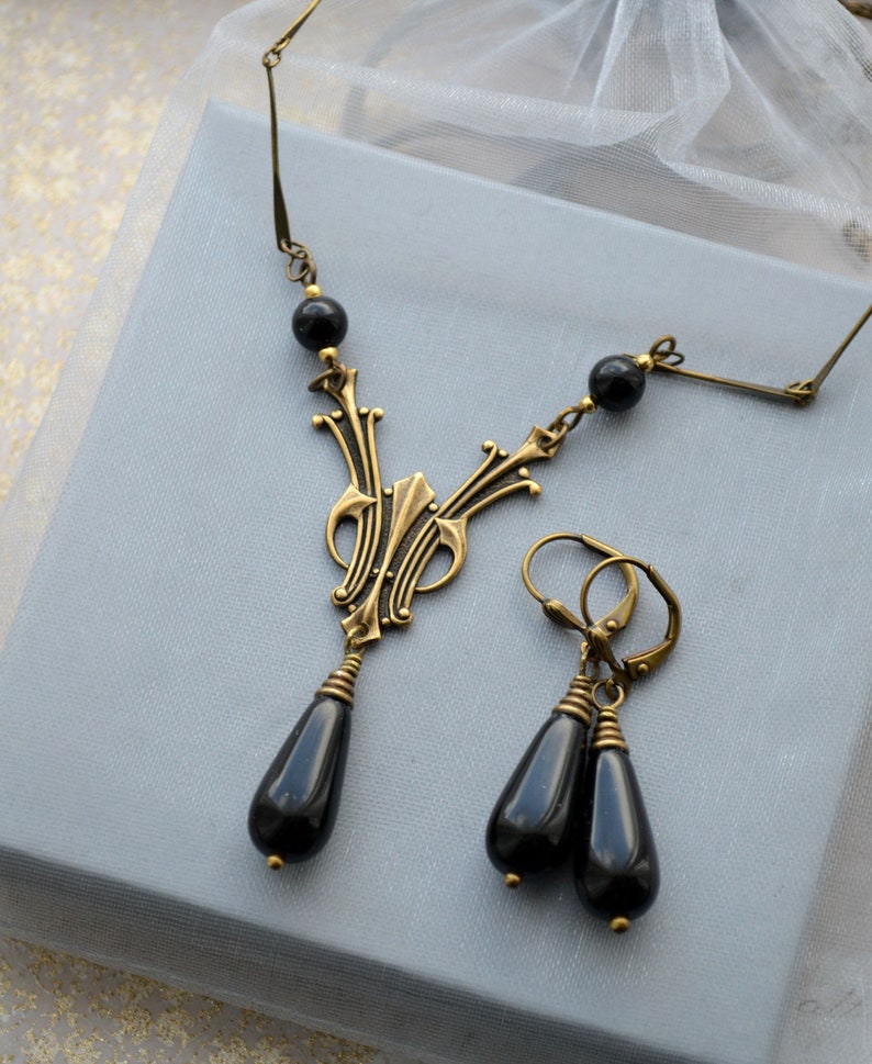 May include: A black onyx necklace and earrings set with a gold-toned pendant featuring an intricate design. The pendant is shaped like a teardrop and hangs from a chain with black onyx beads.