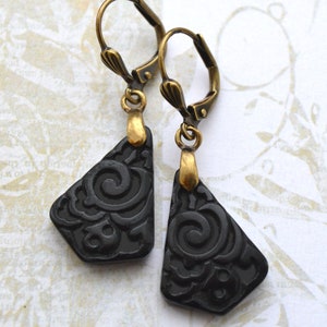 Può includere: Un paio di orecchini pendenti neri con un design a filigrana dorata. Gli orecchini hanno una forma a goccia e presentano un motivo a spirale.