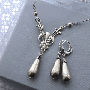 May include: A silver necklace and earrings set with a delicate, ornate pendant and teardrop-shaped earrings.