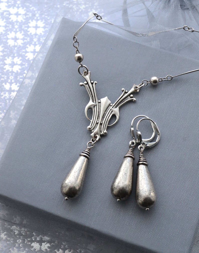 May include: A silver necklace and earrings set with a delicate, ornate pendant and teardrop-shaped earrings.