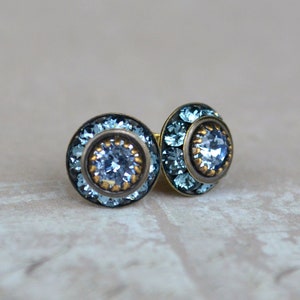 May include: A pair of blue and gold stud earrings with a round, faceted crystal in the center.