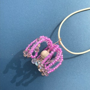 May include: A pink and clear beaded necklace with a white pearl pendant. The necklace is made of small beads and wire.
