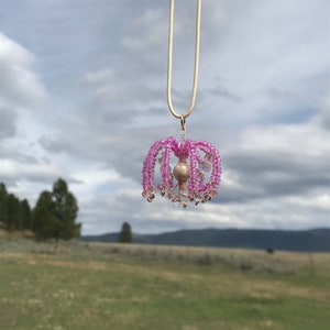 May include: A pink beaded chandelier pendant necklace with a pearl accent hanging from a cream colored cord.