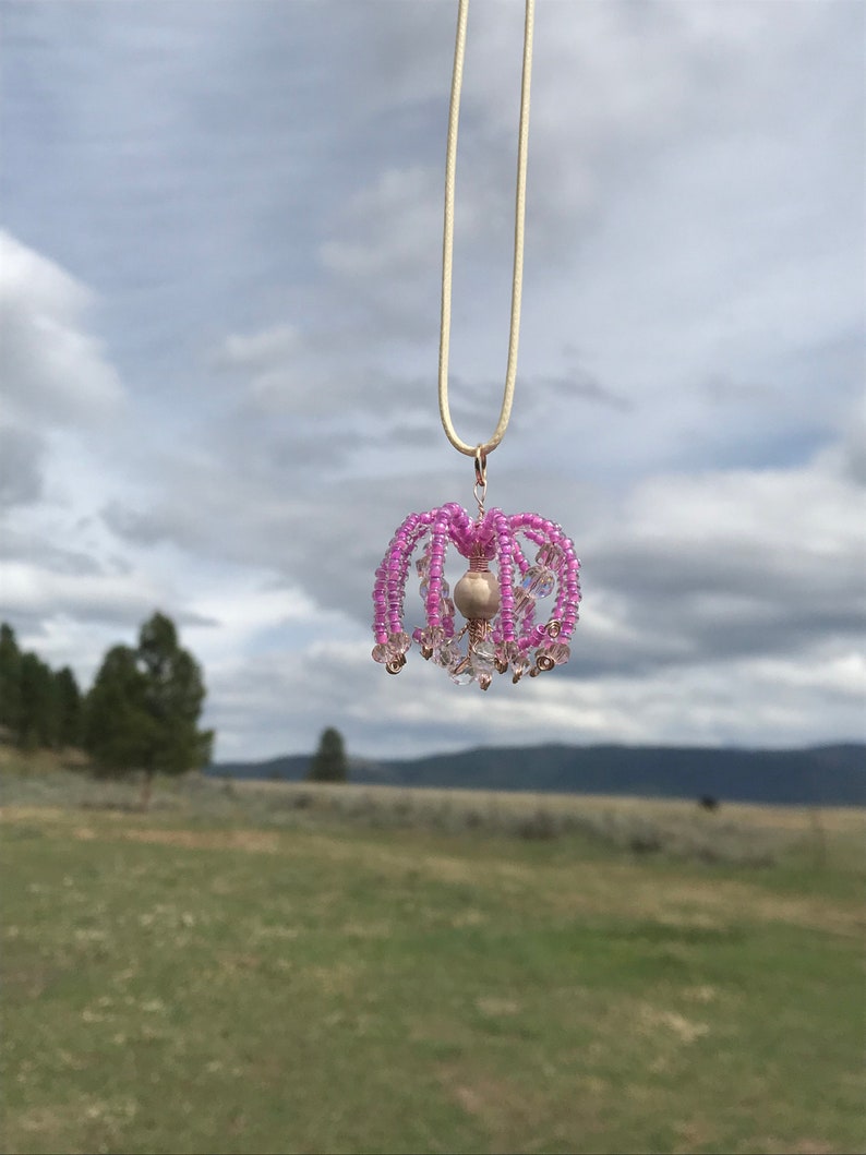 May include: A pink beaded chandelier pendant necklace with a pearl accent hanging from a cream colored cord.