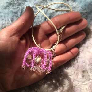 May include: A pink beaded necklace with a white bead pendant. The necklace is on a cream-colored cord.