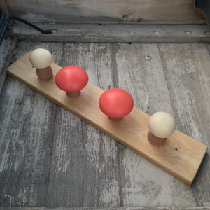May include: A wooden wall-mounted coat rack with four mushroom-shaped hooks. Two hooks are red and two are cream colored.