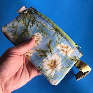May include: A small blue and green zippered pouch with a floral print. The pouch has a strap and a silver ring.