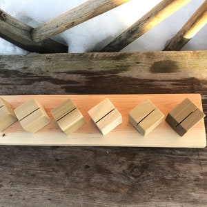 May include: Six wooden place card holders arranged in a row on a wooden board. The holders are made of natural wood and have a rustic look.