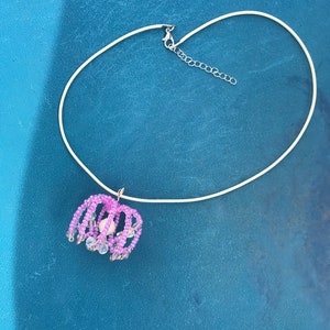 May include: A delicate silver chain necklace with a pink and white beaded pendant. The pendant is shaped like a flower with a pearl in the center.