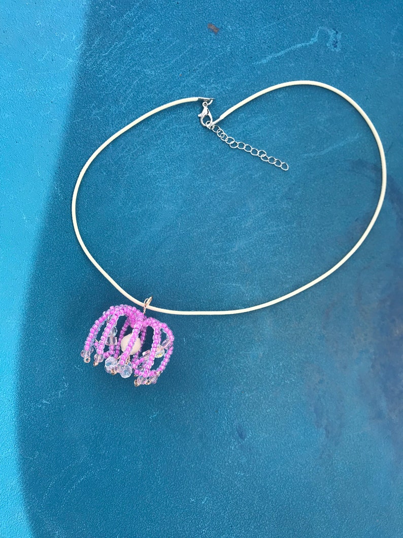 May include: A delicate silver chain necklace with a pink and white beaded pendant. The pendant is shaped like a flower with a pearl in the center.