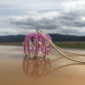 May include: A pink beaded chandelier pendant with a wooden bead in the center and a white cord.