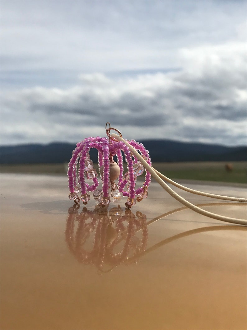 May include: A pink beaded chandelier pendant with a wooden bead in the center and a white cord.
