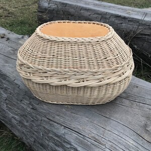 May include: A woven wicker basket with a light brown top and a natural woven finish. The basket is oval shaped and has a rounded bottom.