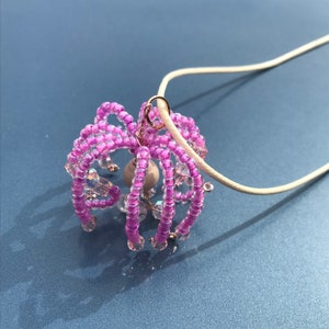 May include: A pink beaded necklace with a delicate pendant featuring a cluster of pink beads and a small wooden bead in the center.