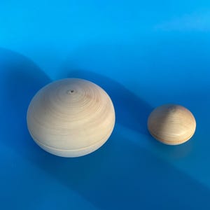 May include: Two wooden bowls, one larger than the other, are shown on a blue background. Both bowls are made of light wood and have a smooth, rounded shape.