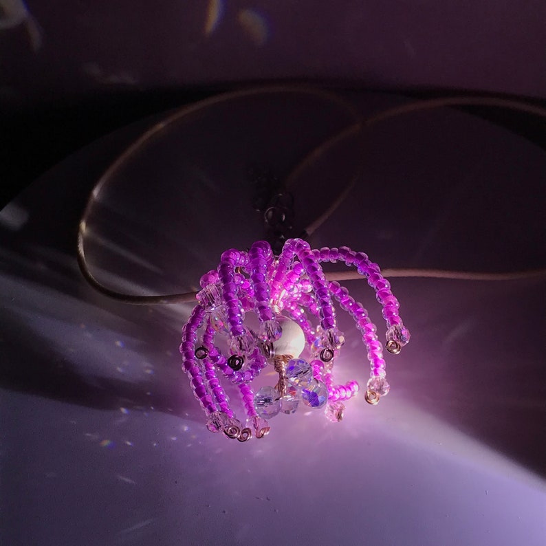 May include: A purple beaded pendant necklace with a white pearl and clear crystal accents. The necklace is hanging from a white cord.