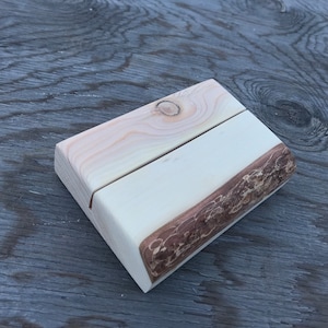 May include: A wooden display stand with a natural wood finish. The stand has a rectangular base and a curved top. The stand is made of two pieces of wood that are joined together.