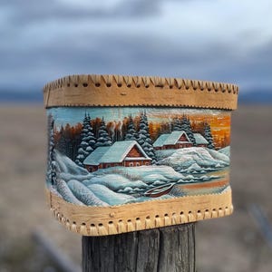 May include: A wooden box with a hand-painted scene of a snowy winter village. The box is decorated with a woven border and has a rustic, vintage look.