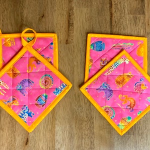 May include: Two pink and yellow quilted pot holders with a colorful animal print. The pot holders have a loop for hanging.