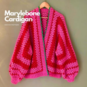 Può includere: Un cardigan all'uncinetto con un vivace motivo a piastrelle granny in filato rosso e rosa alternati. Il capo presenta maniche lunghe, scollo a V e un bordo smerlato verde brillante lungo l'apertura frontale. Il testo recita Marylebone Cardigan CROCHETPATTERN.