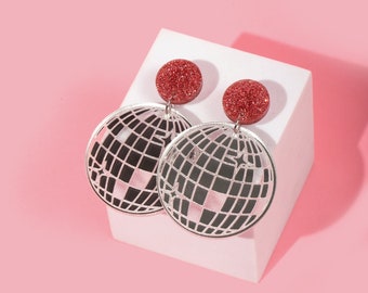 May include: A pair of silver disco ball earrings with red glitter accents. The earrings are dangling and have a circular shape.