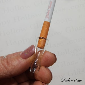 Puede incluir: Un porta cigarrillos de vidrio transparente con un cigarrillo dentro. El cigarrillo está etiquetado como "Golden Harvest".