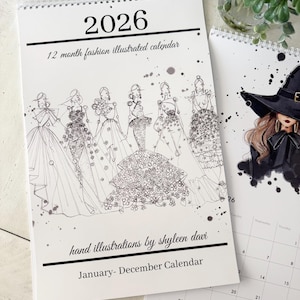 May include: A spiral-bound 2026 calendar featuring fashion illustrations. The cover displays a line drawing of several women in gowns, with the text "12 month fashion illustrated calendar" and "hand illustrations by shyleen davi". A second calendar is partially visible.