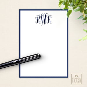 May include: A white notepad with a navy blue border and a navy blue monogram of the letters RWK. A black pen is lying on top of the notepad.