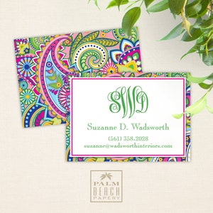May include: A pink and white business card with a green paisley pattern border. The card features a green monogram "SWD" and the text "Suzanne D. Wadsworth (561) 558-2028 suzanne@wadsworthinteriors.com". The bottom of the card has the text "PALM BEACH PAPERY" in black.