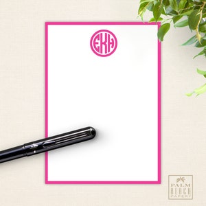 May include: A pink and white stationery set with a pink monogrammed circle in the upper left corner. The monogram is the letters "EKH". The stationery is on a beige background.