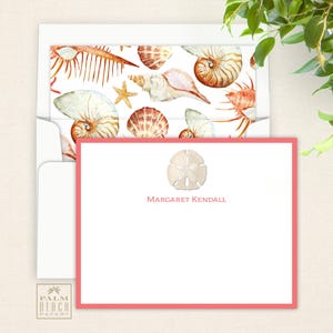 May include: A white card with a pink border and a seashell design. The card has the text "Margaret Kendall" printed on it.