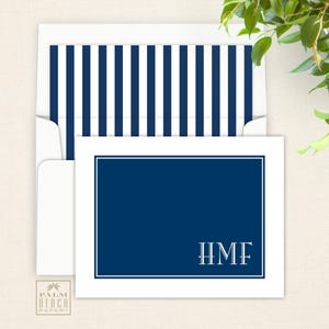 May include: A white card with a blue border and a navy blue rectangle in the center. The rectangle has white letters that spell "HMF" in a serif font.