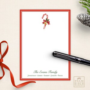 May include: Red and white candy cane with a red bow and gold bells on a white background with a red border. The text "The Evans Family" is printed below the candy cane, followed by the names "Jonathan, Aimee, Sammy, Joseph, Paige".