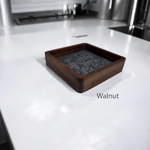 May include: A square wooden tray with a gray felt lining. The tray is made of walnut wood and has a smooth finish. Walnut.