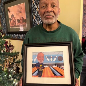 May include: A framed illustration of a person bowling. The person is wearing a green shirt with a blue "M" on it. The bowling alley is blue and orange with a black bowling ball. The illustration is framed in black.