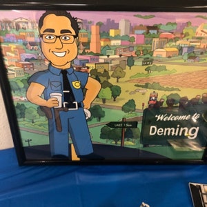 May include: A cartoon illustration of a police officer in a blue uniform holding a cup of coffee. The officer is standing in front of a sign that says "Welcome to Deming". The background is a cartoon cityscape.