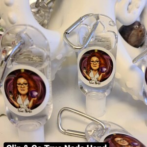 May include: A set of four clear plastic hand sanitizer bottles with a silver clip. Each bottle has a colorful sticker with a cartoon image of a woman and the text "True Node". The bottles are displayed on a white surface with the text "Clip & Go True Node Hand Sanitizer".