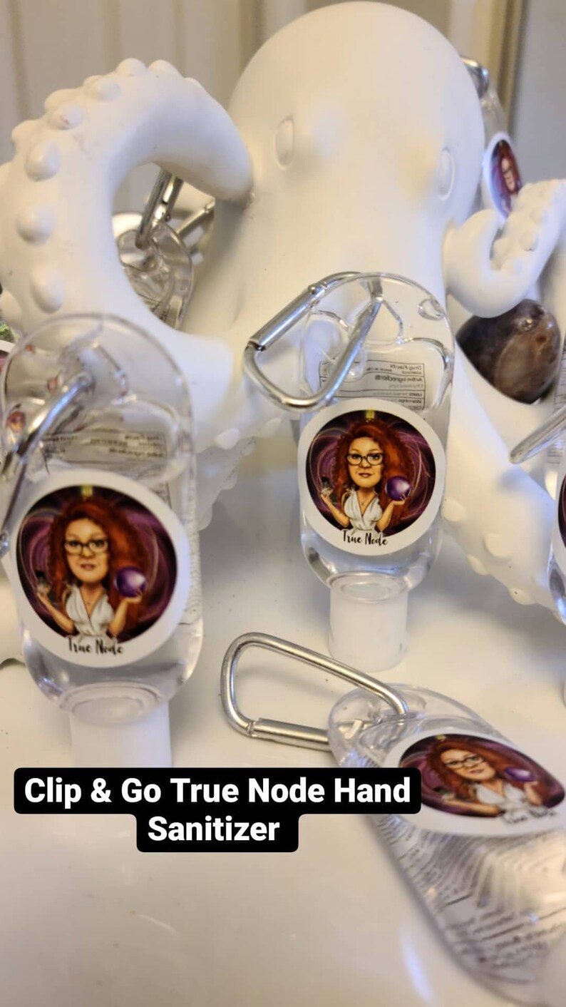May include: A set of four clear plastic hand sanitizer bottles with a silver clip. Each bottle has a colorful sticker with a cartoon image of a woman and the text "True Node". The bottles are displayed on a white surface with the text "Clip & Go True Node Hand Sanitizer".