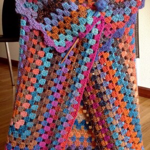 Può includere: Un gilet all'uncinetto colorato con un motivo multicolore. Il gilet è realizzato con una varietà di tonalità di blu, rosa, arancio e marrone.