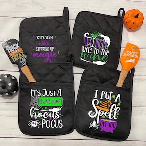 May include: Four black quilted Halloween-themed oven mitts with pockets, each featuring a different spooky phrase in white, green, and purple. Two orange spatulas and two decorative pumpkins complete the festive kitchen set.
