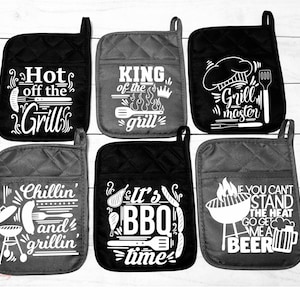 May include: Six quilted oven mitts with various white text designs related to grilling. The mitts are black and gray, with phrases like "Hot off the Grill," "King of the Grill," and "Grill Master."