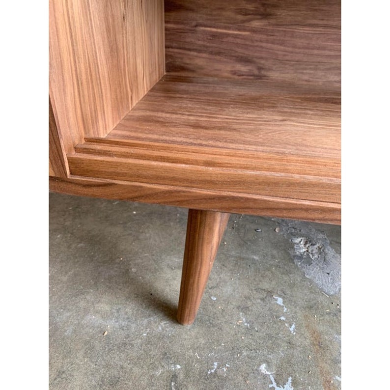May include: A wooden cabinet with a shelf and a single leg visible. The cabinet is made of light brown wood with a natural finish.
