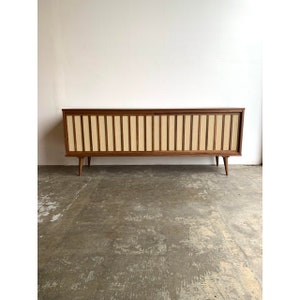 May include: A mid-century modern walnut veneer entertainment console with sliding doors. The doors feature a woven cane panel with a light brown and white pattern. The console has four legs.