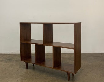 May include: A brown wooden bookshelf with six open shelves and four legs. The bookshelf is standing on a brown floor.
