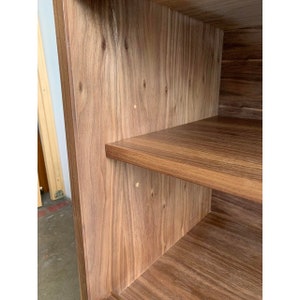 May include: Close-up of the interior of a wooden cabinet with two shelves. The shelves are made of a light brown wood with a smooth finish. The cabinet is made of a darker brown wood with a more textured finish.