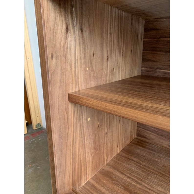 May include: Close-up of the interior of a wooden cabinet with two shelves. The shelves are made of a light brown wood with a smooth finish. The cabinet is made of a darker brown wood with a more textured finish.