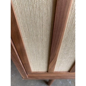 May include: A wooden cabinet with a woven fabric panel. The cabinet has a dark brown finish and a simple design.