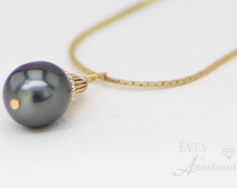 Può includere: Una collana d'oro con un pendente di perla grigio scuro. La perla ha una lucentezza lucida e un piccolo dettaglio dorato. La catena è in oro fine e strutturato. La collana è presentata su uno sfondo bianco.